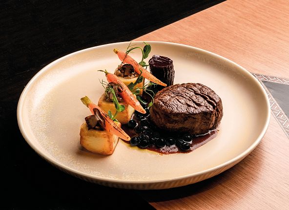 Une assiette claire sur laquelle repose un morceau de viande, joliment agrémenté de légumes et d'une sauce.