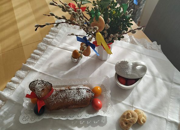 Ein gebackenes Lamm, Ostereier in einer Schale, ein Strauß Frühlingszweige und Tischdecke. Feierliche Osterdekoration auf einem Tisch.