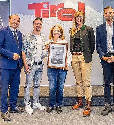 Fünf Personen posieren mit einer Auszeichnung vor einem 'Tirol'-Logo. Die Frau in der Mitte hält die Auszeichnung, alle lächeln freundlich.