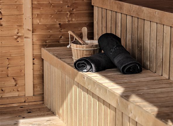 Sauna-Interieur aus Holz mit einem Holzeimer und dunklen Handtüchern auf einer Bank, ideal für Entspannung.