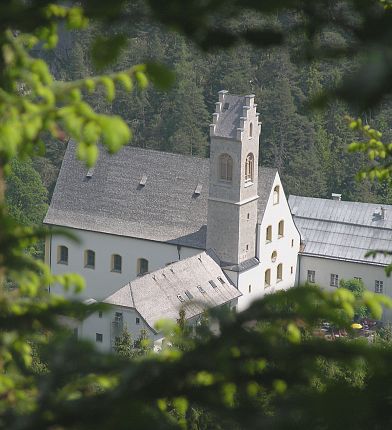Ein idyllisches Kloster im Wald, umgeben von üppigem Grün und mit einem markanten Turm, der sich über die Dächer erhebt.