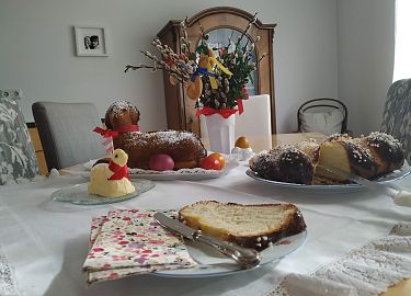 Ein festlich gedeckter Tisch mit Ostergebäck wie Hefezopf und Osterlämmern, dekoriert mit bunten Ostereiern und Buttervögeln.