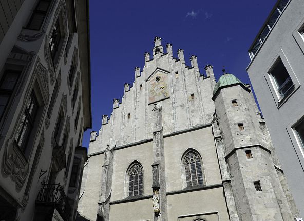 Gotische Kathedrale mit spitzbogigen Fenstern, flankiert von modernen Gebäuden, vor einem strahlend blauen Himmel.