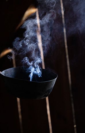 Schwarze Räucherschale mit aufsteigendem Rauch vor dunklem, holzgetäfeltem Hintergrund.