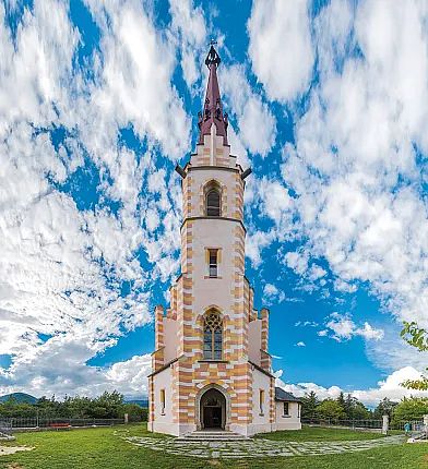 Imposanter Kirchturm vor blauem Himmel mit weißen Wolken, detailreiche Architektur erkennbar.