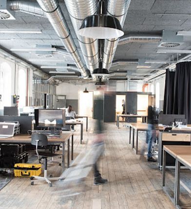 Modernes Büro mit mehreren Schreibtischen und Personen, die an Computern arbeiten. Eine Person bewegt sich schnell durch den Raum.